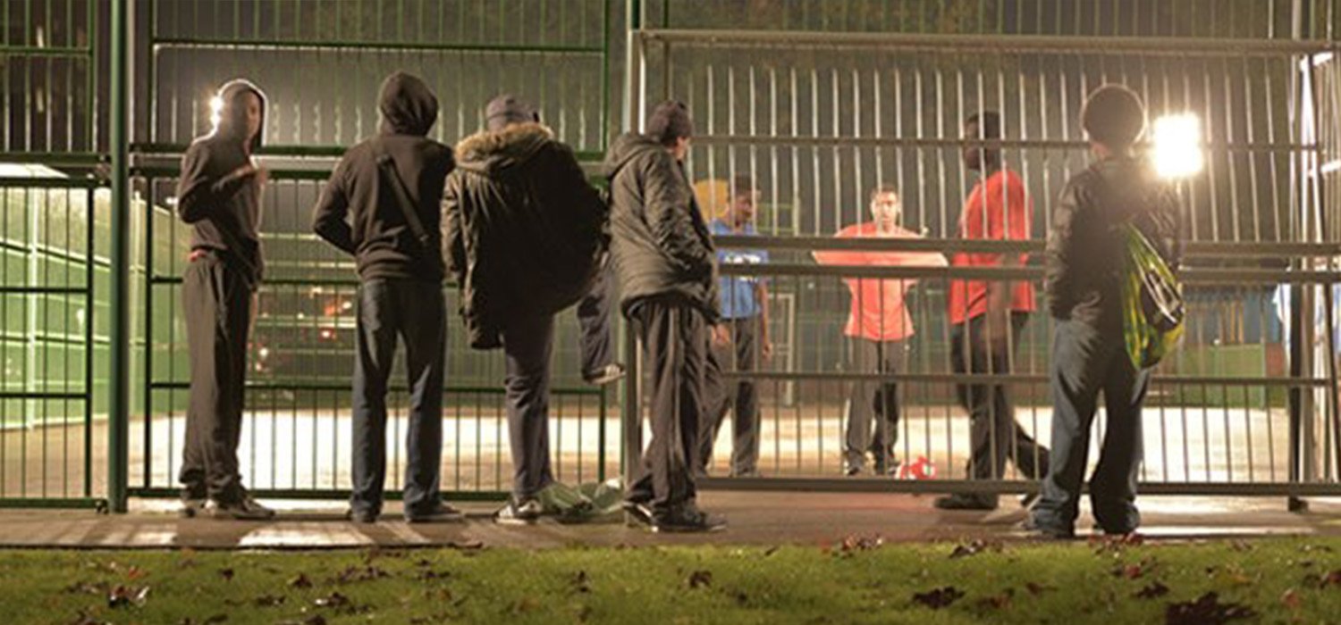 young people standing by gated football pitch