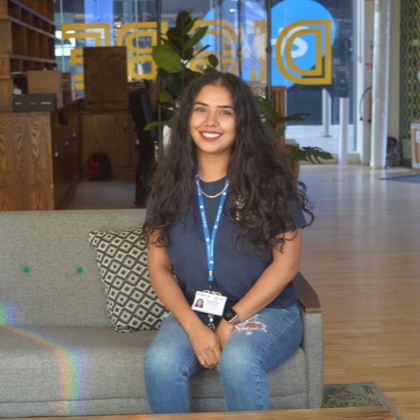 Picture of a person sat down on a grey sofa, smiling.